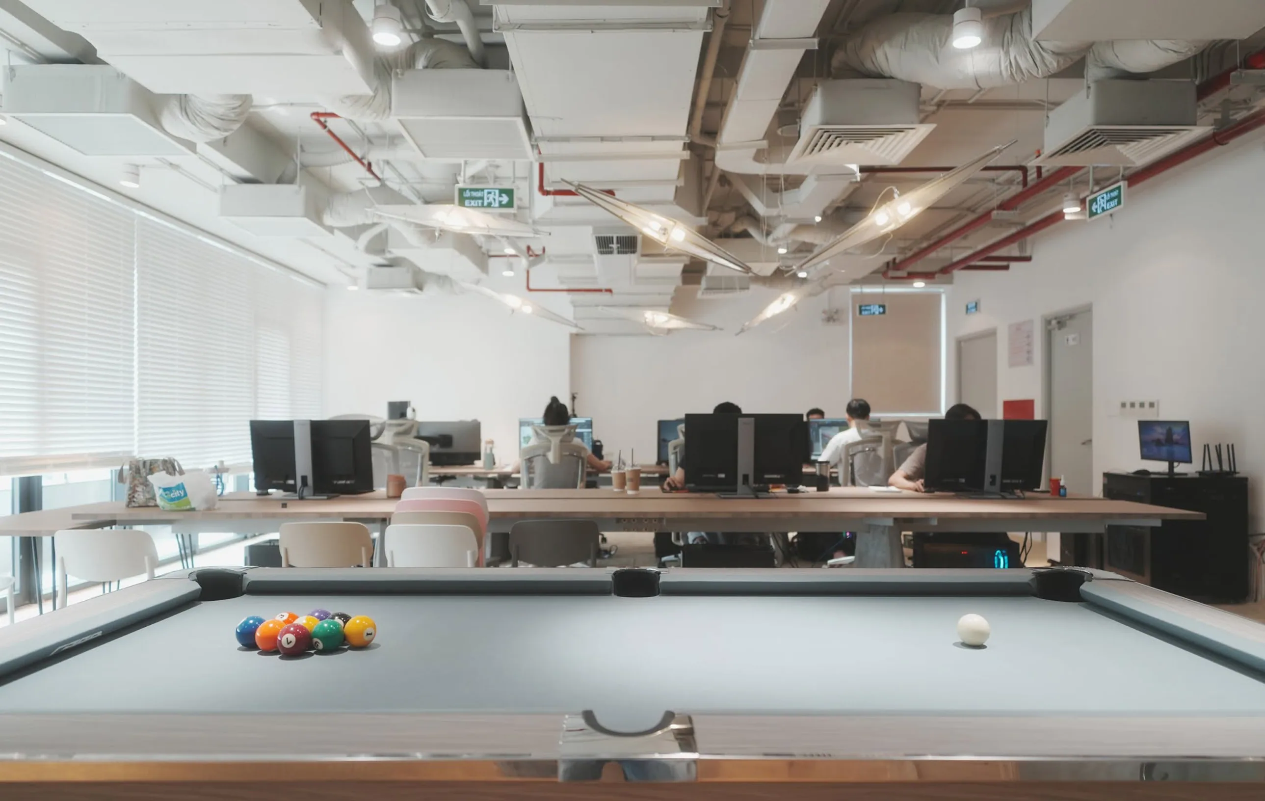 The NRTRS studio — a billiard table in the foreground, the team at a long shared desk of workstations beyond, ductwork and lighting exposed overhead